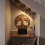 Tree of life wall art above a wood desk in a cozy under-stair home office with laptop and chair