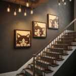 Wood wall art featuring playful cat designs hangs above a staircase in a stylishly lit entryway.