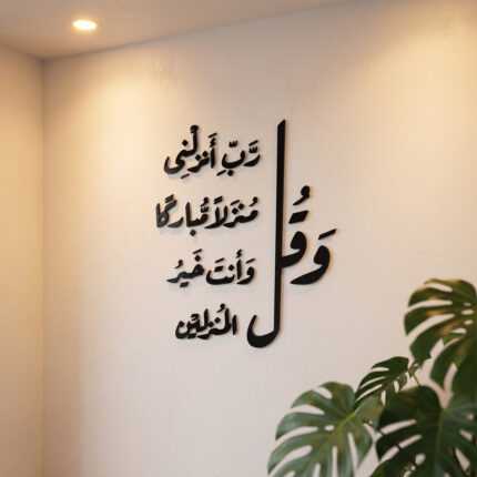 Islamic wall art with black Arabic calligraphy displayed on a softly lit interior wall beside monstera leaves