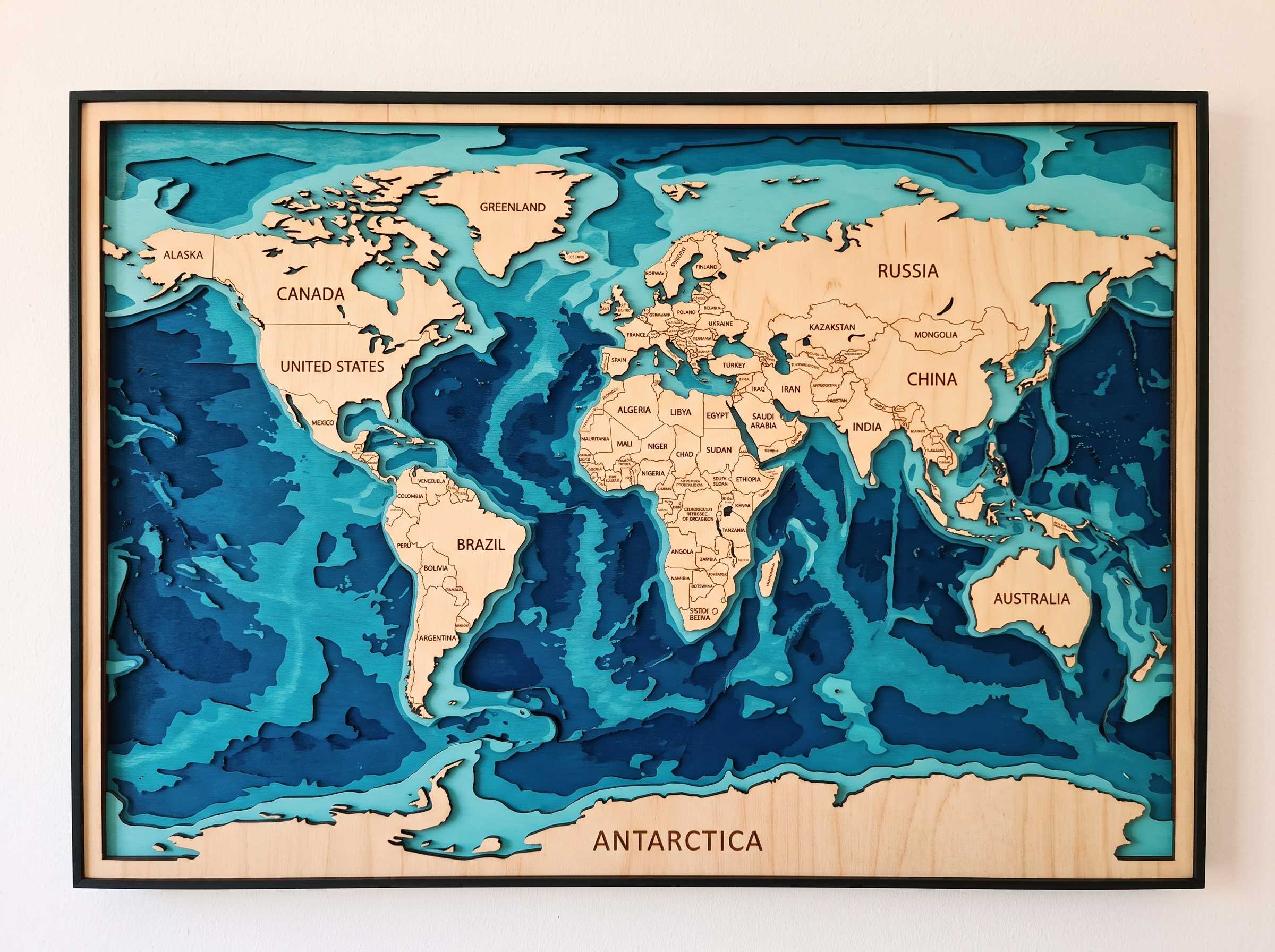 Gemini_Generated_Image_v8ert6v8ert6v8er World map wall art in layered blue wood with engraved country names and black frame